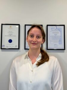 Portrait photo of Alison Glaister standing in front of certificates on a wall.