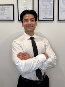 Portrait photo of Martin Solon standing in front of certificates on a wall.